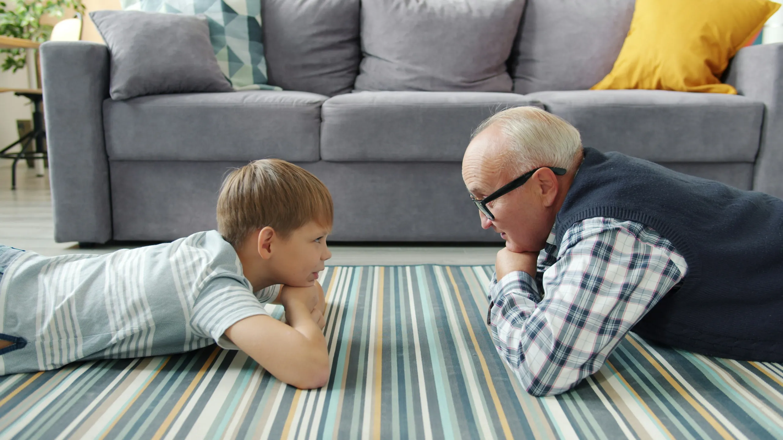 A grandfather and grandson lying on the rug, smiling at each other